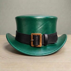 Peut inclure: Un chapeau haut de forme en cuir vert avec une bande noire et une boucle de couleur or. Le chapeau a un large bord et une couronne cylindrique. Le chapeau est probablement un déguisement ou un article fantaisie.