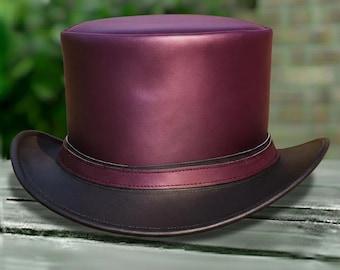 Puede incluir: Un sombrero de copa burdeos con ala marrón oscuro. El sombrero presenta una banda de cuero burdeos con una fina línea blanca. El sombrero está hecho de un material liso y brillante.