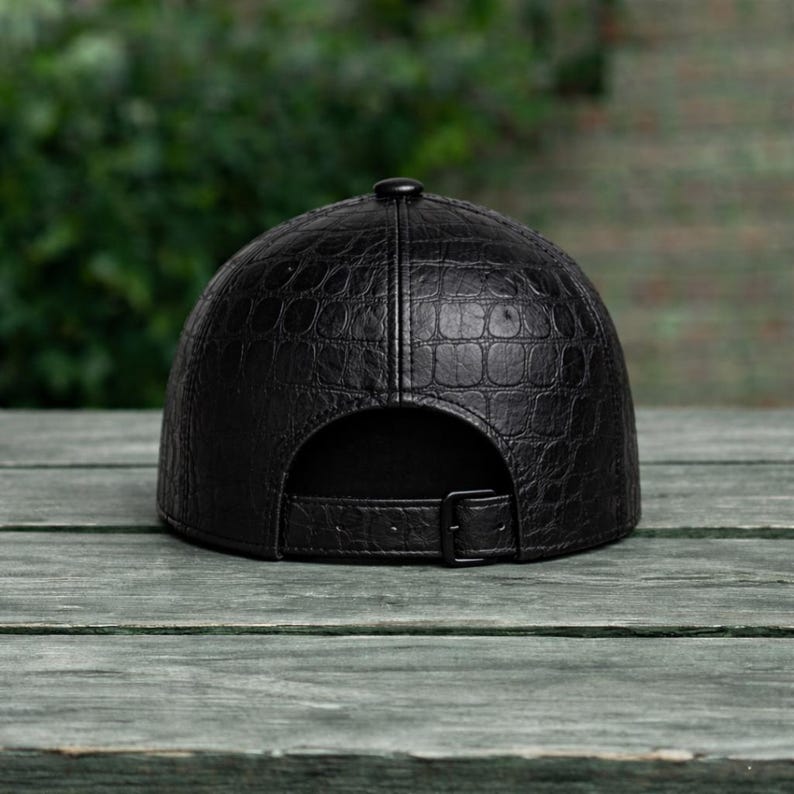 K&ouml;nnte beinhalten: Schwarze Baseballkappe mit strukturiertem, krokodil&auml;hnlichem Muster. Die Kappe hat einen gebogenen Schirm, einen Knopf oben und einen verstellbaren Riemen mit Schnalle hinten. Aus Leder.