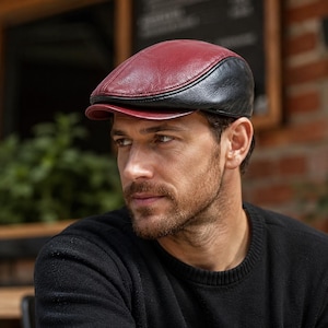 Könnte beinhalten: Zweifarbiges Leder-Newsboy-Cap. Die Kappe hat eine bordeauxfarbene Krone und Krempe mit einem schwarzen Oberteil. Ein klassischer Stil, der für verschiedene Anlässe geeignet ist. Hergestellt aus glattem, geschmeidigem Leder.