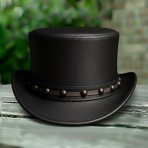 May include: A black top hat with a wide brim and a decorative band featuring small, dark metal studs. The hat is made of a textured material, likely leather, and sits on a light-colored surface.