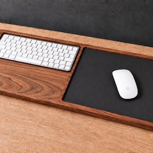 Puede incluir: Una bandeja organizadora de escritorio rectangular de madera con una ranura empotrada para un teclado inalámbrico blanco a la izquierda y una superficie de alfombrilla de ratón rectangular negra a la derecha, con un ratón blanco encima.