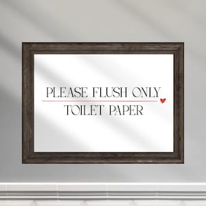 Può includere: Un cartello incorniciato con la scritta "PLEASE FLUSH ONLY TOILET PAPER" in nero, con un cuore rosso. La cornice è di colore marrone scuro. Il cartello è appeso a una parete bianca sopra piastrelle bianche.