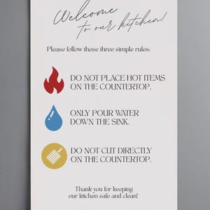 May include: A white kitchen sign with black script that reads "Welcome to our kitchen!" and three rules: no hot items, only pour water in the sink, and no cutting on the countertop. A decorative piece for the kitchen.
