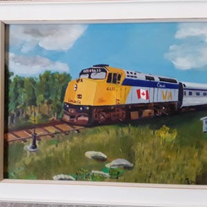 Puede incluir: Pintura al óleo de un tren VIA Rail amarillo, azul y plateado con la bandera canadiense en el lateral. El tren está sobre una vía en un campo de hierba con árboles y un cielo azul con nubes. La pintura está en un marco blanco.