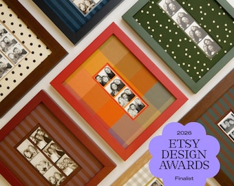 May include: A collection of rectangular picture frames in various colors including red, dark blue, green, and light wood, each containing a vertical strip of black and white photo booth portraits mounted on patterned backgrounds like polka dots and stripes.