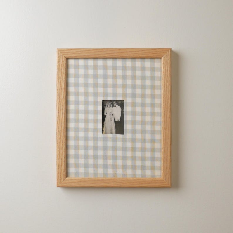 Pu&ograve; includere: Una fotografia incorniciata con un'immagine in bianco e nero di una coppia. La cornice &egrave; in legno chiaro e lo sfondo &egrave; un motivo a scacchi blu, grigio e bianco.