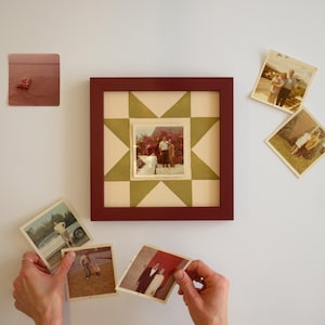 May include: A square dark red picture frame containing a cream and olive green star-patterned mat with a central photograph of two people. Surrounding the frame are five loose vintage square photographs depicting various outdoor scenes and people.