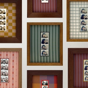 May include: A collection of framed photo strips, each containing multiple images of people. The frames are various sizes and feature different patterned backgrounds, including gingham, stripes, and floral designs. The frames are made of wood.