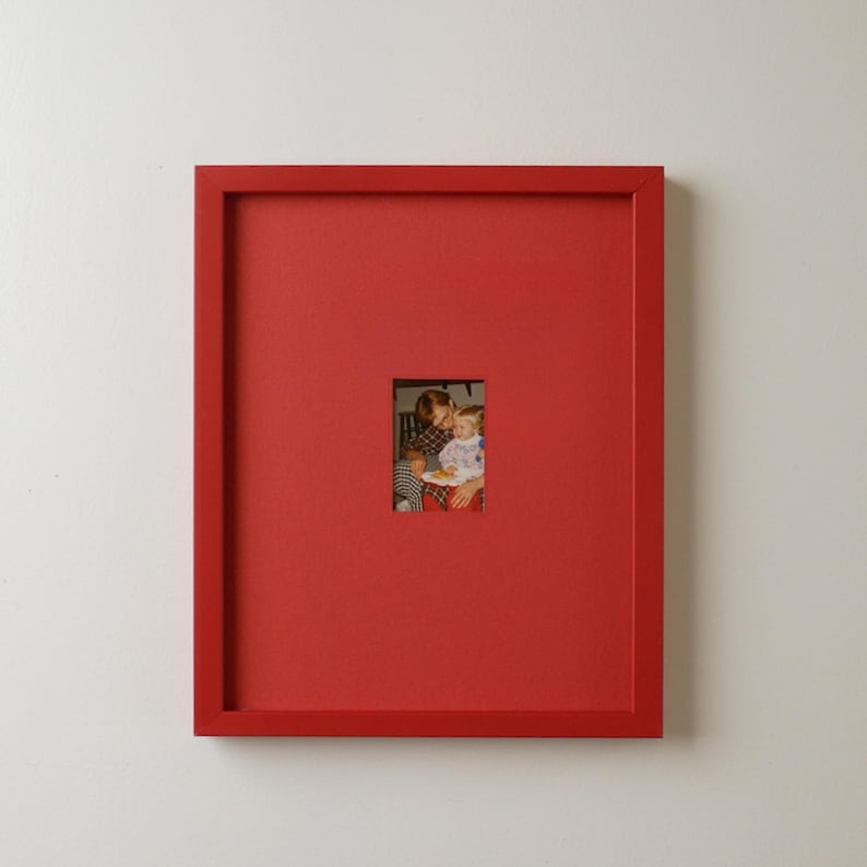 Pode incluir: Uma moldura vermelha com uma pequena fotografia no centro. A fotografia mostra uma pessoa segurando uma crian&ccedil;a. A moldura &eacute; de uma cor vermelha s&oacute;lida e vibrante.