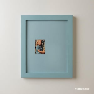 Op de afbeelding: Een vierkante, vintage blauwe fotolijst met een kleine foto van een kind. De lijst heeft een effen, lichtblauwe kleur en de foto is gecentreerd in de lijst. De tekst "Vintage Blue" staat rechtsonder.