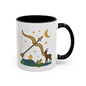 May include: White ceramic mug with a black interior and handle. The mug features a gold bow and arrow, a deer, stars, a crescent moon, and a candle design. The mug is a standard 325 ml size.