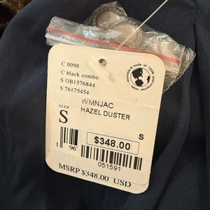 May include: A tag for a Hazel Duster in black combo, size small. The tag includes the product code, size, and a price of $348.00. The tag is attached to a dark blue garment.