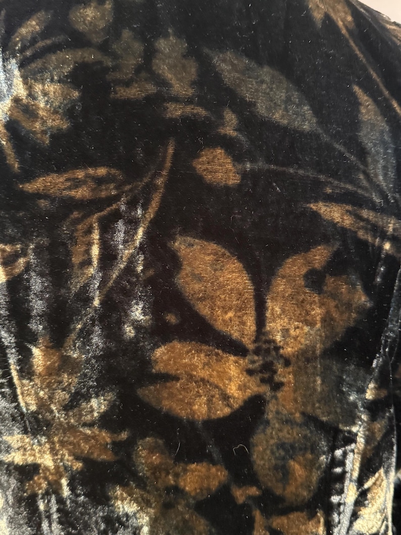 May include: Close-up of a black velvet fabric with a floral pattern in shades of brown and gold. The design features large, stylized flowers and leaves, creating a rich, textured appearance.