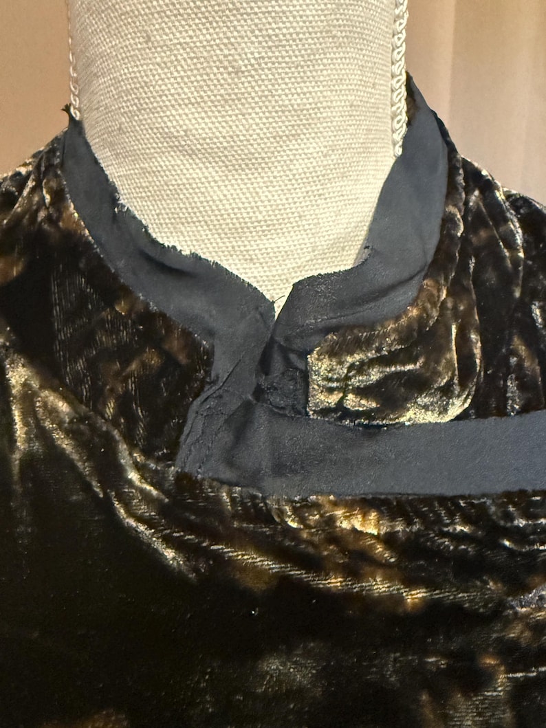 May include: Close-up of a dark brown velvet garment with a black collar. The velvet has a subtle sheen and a textured appearance. The collar is a contrasting black fabric. The garment is displayed on a mannequin.
