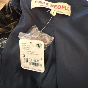 May include: A black and brown velvet duster coat with a navy blue lining. The tag reads "FREE PEOPLE" and "HAZEL DUSTER". The size is small. The tag also includes the text "MADE IN INDIA".