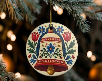 May include: A round ceramic ornament featuring a central bell illustration decorated with red tulips, blue flowers, and green foliage. The design includes geometric patterns in red and gold on a cream background, suspended by a gold cord.