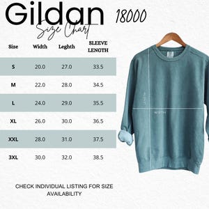 May include: A teal crewneck sweatshirt hanging on a wooden hanger next to a Gildan 18000 size chart. The chart lists sizes S through 3XL with corresponding width, length, and sleeve length measurements in inches. Text reads: Gildan 18000 Size Chart.