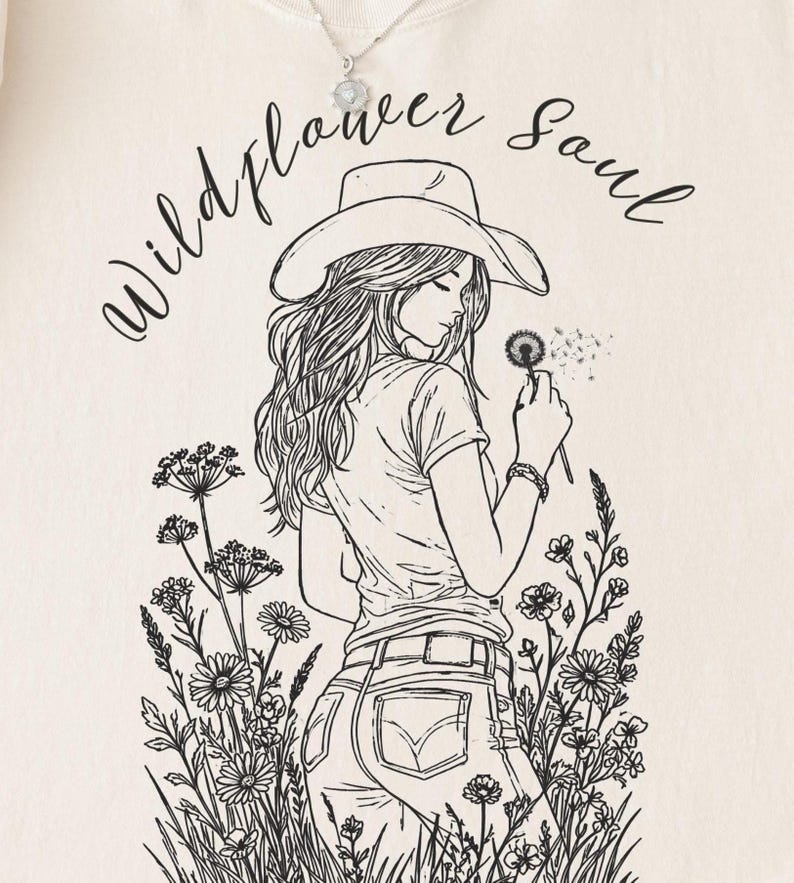 Puede incluir: Sudadera color crema con una ilustraci&oacute;n en blanco y negro de una mujer con sombrero de vaquero sosteniendo un diente de le&oacute;n. El texto "Wildflower Soul" est&aacute; arqueado sobre la ilustraci&oacute;n.