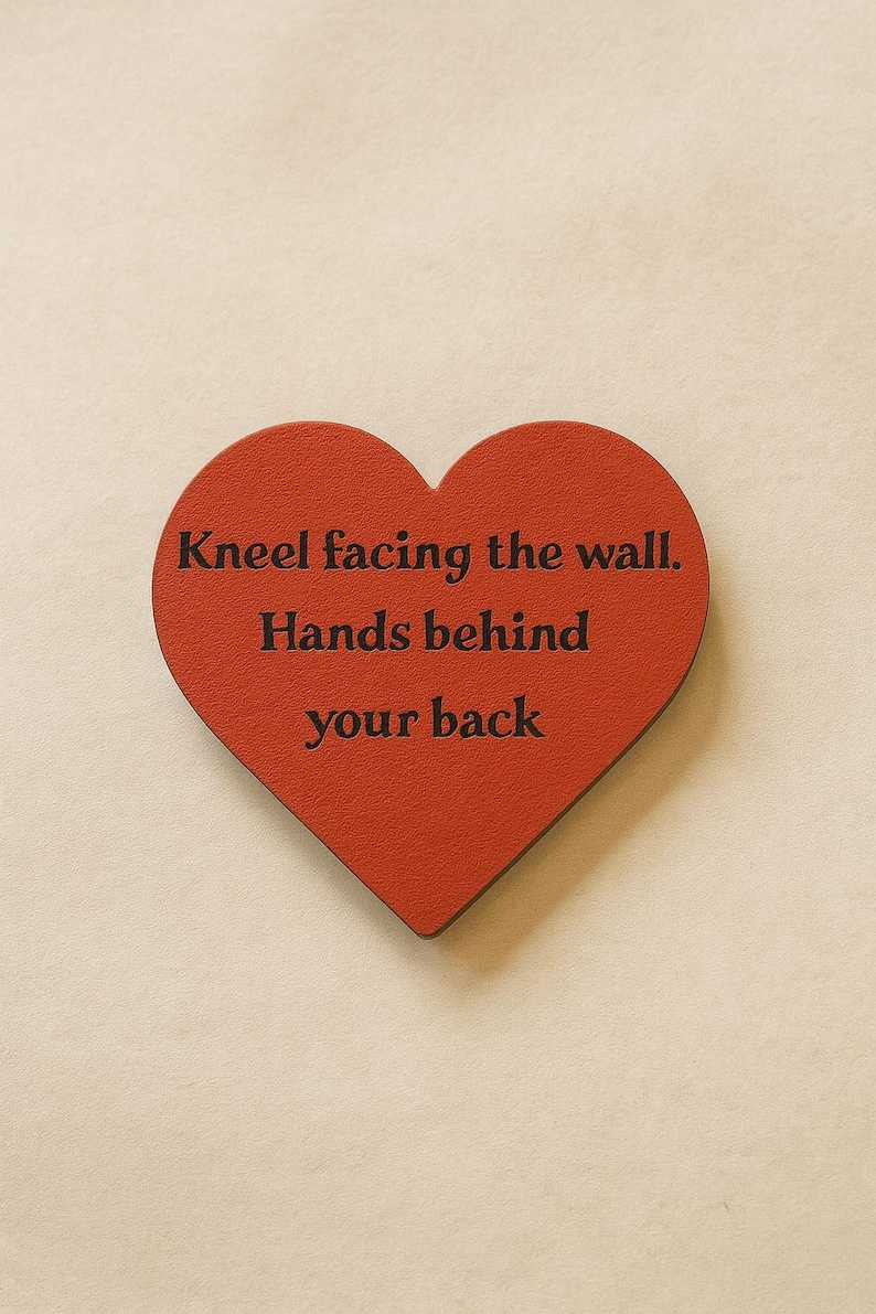 Może przedstawiać: Czerwony przedmiot w kształcie serca z czarnym napisem "Kneel facing the wall. Hands behind your back". Obiekt znajduje się na neutralnym tle.