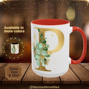 Può includere: Tazza in ceramica bianca con interno e manico rossi. La tazza presenta la lettera "P" dorata con un design botanico di foglie verdi e dettagli dorati. È visibile anche il testo "Disponibile in più colori" e "Misure 325 ml e 444 ml".