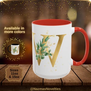 May include: White ceramic mug with a red interior and handle. The mug features a gold letter "W" with green and gold botanical accents. The mug is available in 312ml and 425ml sizes. The text "Available in more colours" is also visible.