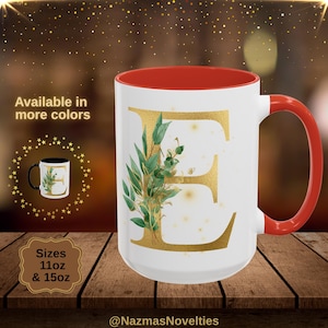 May include: White ceramic mug with a red interior and handle, featuring a gold letter "E" design with green leaves. The mug is available in 312ml and 425ml sizes. Text on the image says "Available in more colours".