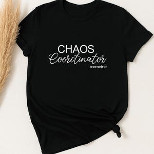 May include: Black t-shirt with the words "CHAOS Coordinator" in white script and sans-serif font. The text "#cometrie" is below the main text. The shirt is knotted at the bottom.