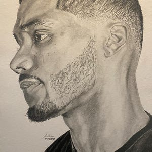 May include: A detailed pencil drawing of a man's profile, showcasing his face and upper torso. The artwork highlights the man's short, textured hair, beard, and the shadows that define his features. The drawing is signed and dated.