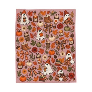 May include: A rectangular blanket featuring a repeating pattern on a dusty pink background. The design includes white ghosts wearing orange beanies, orange pumpkins, brown boots, plaid bows, candles, books, and coffee cups with autumn leaves.