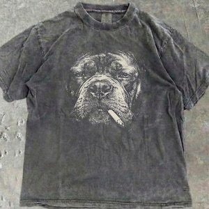 May include: A dark grey t-shirt with a graphic print of a dog smoking a cigarette. The dog's face is the central focus, with the cigarette adding a rebellious touch. The t-shirt has a faded, vintage appearance.