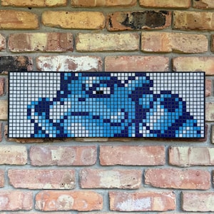 Puede incluir: Una pieza de arte mural de mosaico rectangular que presenta un gráfico pixelado de la cara de un bulldog azul. El diseño está compuesto por pequeños azulejos cuadrados en varios tonos de azul, blanco y negro, dispuestos para formar al can.