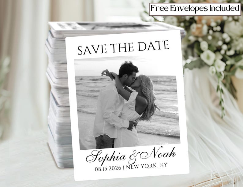 May include: A stack of white "Save the Date" cards featuring a black and white photo of a couple kissing on a beach. The cards include the names "Sophia & Noah" and the date "08.15.2026 | NEW YORK, NY". Text at the top reads "Free Envelopes Included".