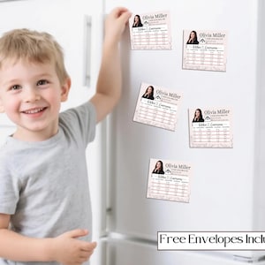 May include: A young child smiles while reaching for a magnet on a white refrigerator. The magnets feature a headshot of a woman and the text "Olivia Miller, Realtor." The phrase "Free Envelopes Included" is printed at the bottom.