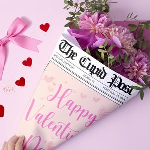 Peut inclure: Un bouquet de pivoines roses envelopp&eacute; dans un c&ocirc;ne en forme de journal avec le titre "The Cupid Post" et le texte "Happy Valentine's Day". L'arrangement comprend un n&oelig;ud rose et des confettis en forme de c&oelig;ur rouges sur fond rose.