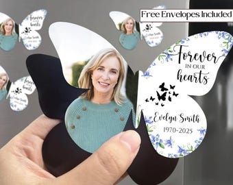 May include: Butterfly-shaped memorial magnets featuring a photo of a woman in a teal sweater. The magnets have black wings and white wings with the text "Forever in our hearts" and the name "Evelyn Smith 1970-2025".