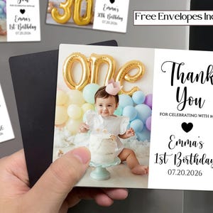 May include: A photo magnet featuring a baby celebrating their first birthday. The magnet includes the text "Thank You" and "Emma's 1st Birthday 07.20.2026". The baby is surrounded by balloons and a cake. The words "Free Envelopes Included" are also visible.