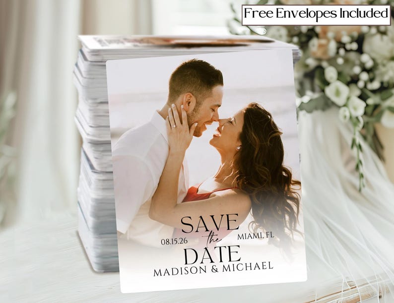 May include: A stack of save-the-date cards featuring a couple embracing on a beach. The cards have the text "Save the Date" with the date 08.15.26 and the names Madison & Michael, Miami, FL. The words "Free Envelopes Included" are in the top right corner.