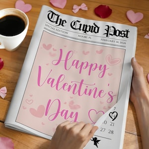 Peut inclure: Un journal intitul&eacute; "The Cupid Post" avec le titre "Happy Valentine's Day" en script rose. Le journal est entour&eacute; de coeurs roses, de p&eacute;tales de rose, de noeuds et d'une tasse de caf&eacute; sur une surface en bois.