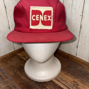 Puede incluir: Gorra roja de estilo vintage con visera plana. Presenta un parche blanco y rojo con la palabra "CENEX" en letras blancas. La gorra se exhibe sobre una cabeza de maniquí blanca.