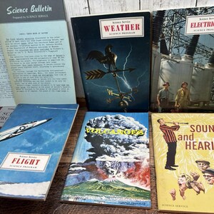 May include: A collection of vintage science books with colorful covers. Titles include "Science Bulletin," "Weather," "Electricity," "Flight," "Volcanoes," and "Sound and Hearing." The books feature illustrations and text related to scientific topics.