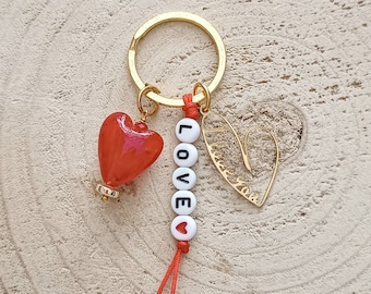 May include: A gold key chain with a red heart charm, a white bead charm with the word "LOVE" spelled out, and a gold heart charm with the words "I love you" inscribed.