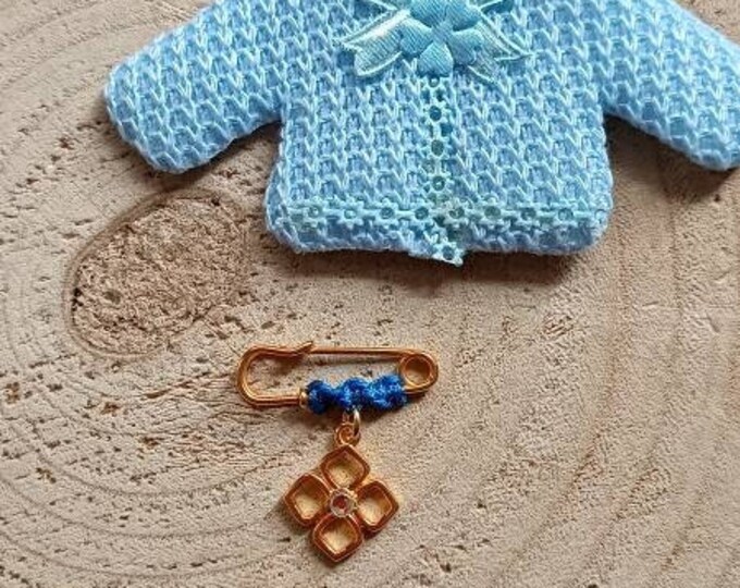 Golden sparkling mini cross brooch on a blue sweater cushion