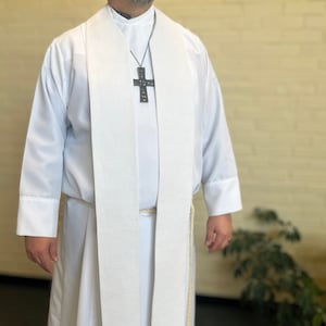 May include: White clergy stole with a black cross pendant. The stole is made of a lightweight fabric and has a simple design.