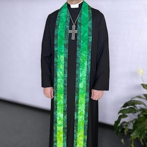May include: A black clergy robe with a green and black patterned stole. The stole has vertical stripes of green and black fabric. A silver cross pendant hangs from a chain around the neck.