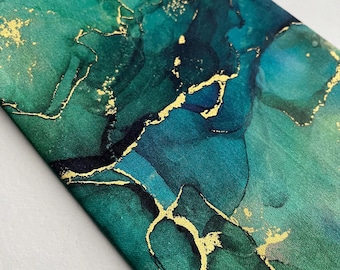 Puede incluir: Primer plano de una tela con un diseño abstracto. La tela presenta tonos de verde y turquesa con detalles dorados. Los detalles dorados crean un efecto veteado, con vetas y motas en todo el diseño. La tela probablemente se utiliza para moda o decoración del hogar.