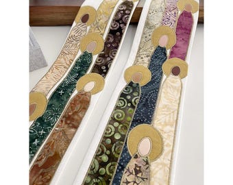 May include: Two white fabric stoles with gold trim and colorful fabric appliques of figures with halos. The figures are arranged in a vertical line and are made of different patterned fabrics.