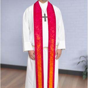 May include: A white robe with a vibrant red and orange stole. A silver cross pendant hangs from a necklace. The stole has vertical stripes of red and orange. The robe has long sleeves.