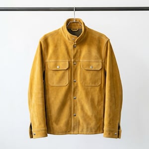 May include: A mustard yellow suede jacket featuring a stand-up collar, long sleeves with buttoned cuffs, and a front placket with silver-toned metal snap buttons. The garment includes two chest pockets with snap-button flaps and a smooth texture.