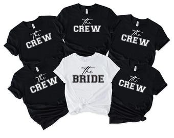 May include: A collection of black and white t-shirts. Five black shirts display "The Crew" in white block letters, while one white shirt reads "The Bride" in black block letters. All shirts have a crew neck.